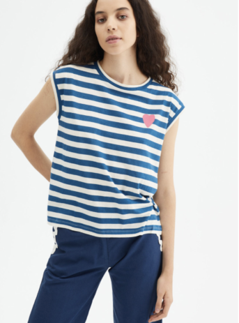 Camiseta básica blanca de algodón con estampado de rayas azules con detalle de corazón. Con cuello redondo y sin mangas. La modelo mide 179 cm y lleva la talla S.