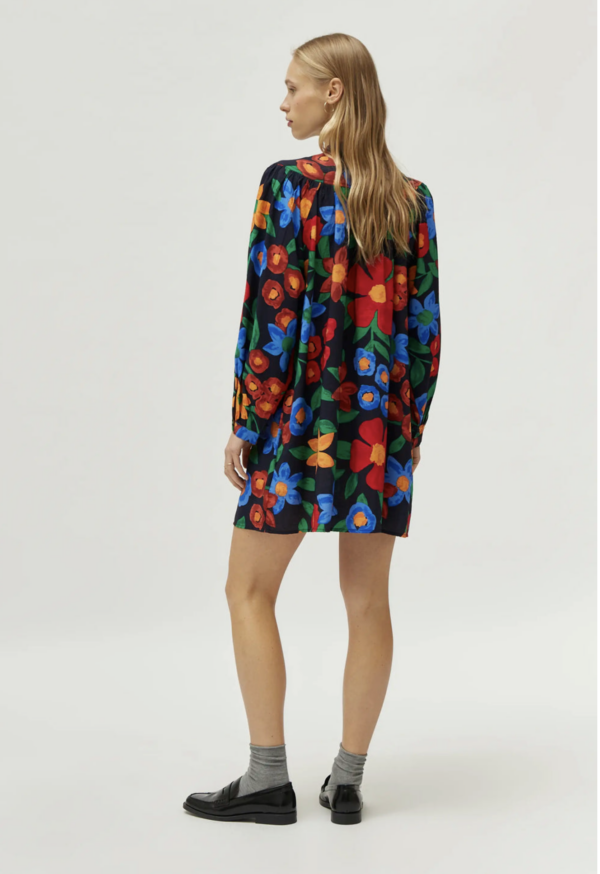 Vestido corto en crepé de viscosa con estampado de flores multicolor. Con cuello mao y manga larga. Cierre frontal con botones. Detalle de corte en el pecho.