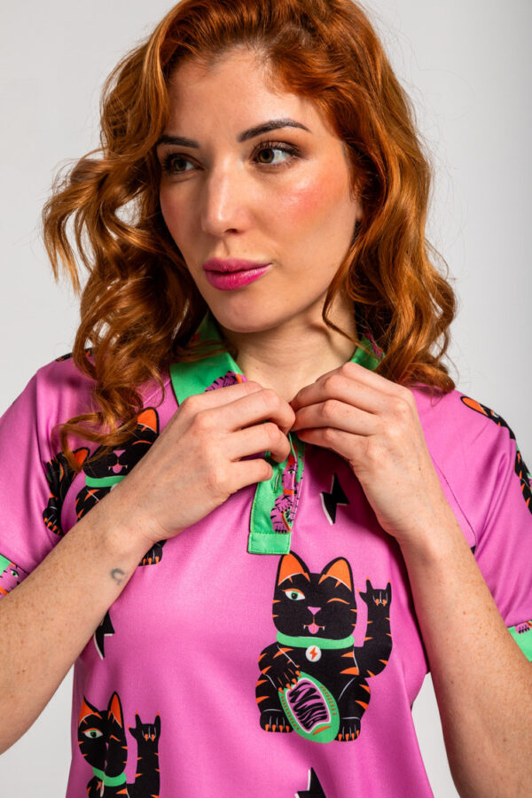 Polo de color rosa y cuello verde, con estampado de gato de la suerte. También puedes encontrarla en nuestra tienda física en el Casco Antiguo de Badajoz.