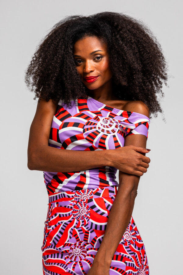 Top asimétrico Hola Caracola, estampado geométrico en lilas, rojos y blancos, con frunces y escote de un solo hombro. Disponible en Dulce Locura.