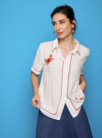 Camisa blanca con ribetes rojos y cangrejo bordado, diseño vintage con estilo unisex. Disponible en Dulce Locura, tienda de moda en Badajoz.