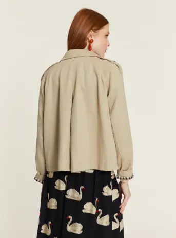 Gabardina corta de color beige con forro de cuadros. Disponible en Dulce Locura, tienda de moda en Badajoz.