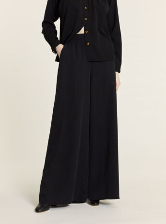 Pantalón fluido Tencel negro palazzo de pierna ancha y caída recta con cintura ajustada y bolsillos laterales. Disponible en Dulce Locura, tienda de moda en Badajoz.
