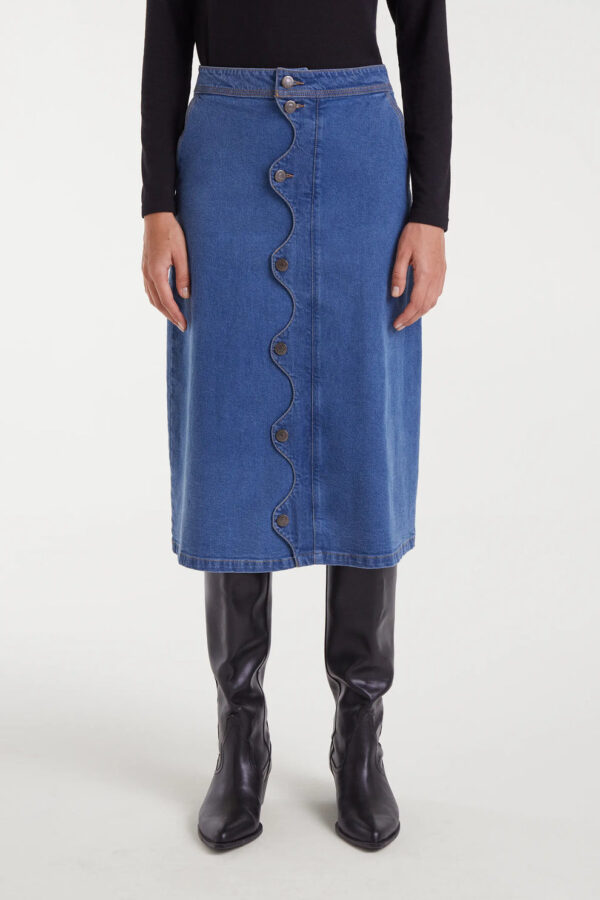 Falda midi azul de tejido denim elástico con tiro alto, cierre frontal de botones y detalle ondulado. Disponible en Dulce Locura, tienda de moda en Badajoz.