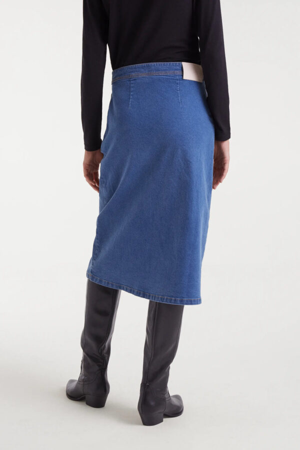 Falda midi azul de tejido denim elástico con tiro alto, cierre frontal de botones y detalle ondulado. Disponible en Dulce Locura, tienda de moda en Badajoz.