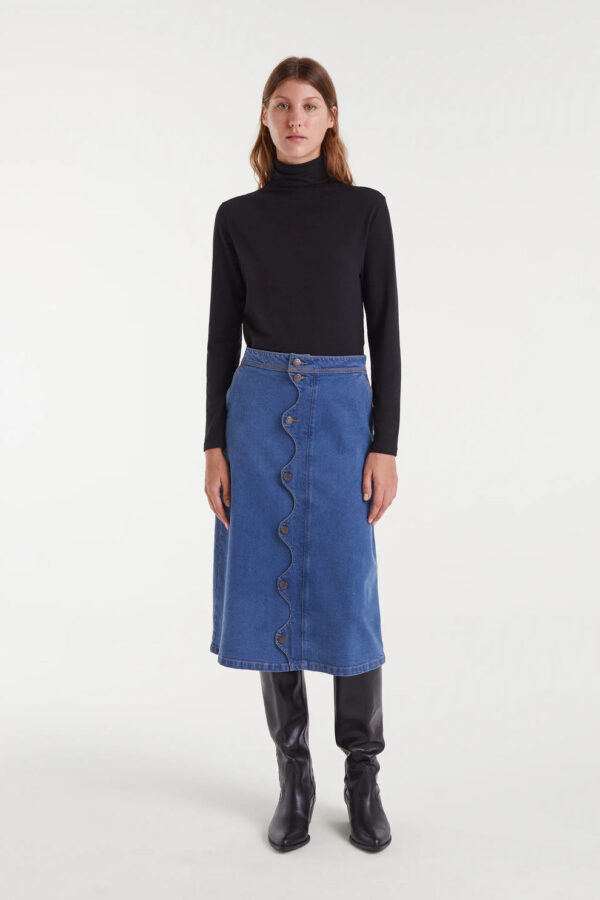 Falda midi azul de tejido denim elástico con tiro alto, cierre frontal de botones y detalle ondulado. Disponible en Dulce Locura, tienda de moda en Badajoz.